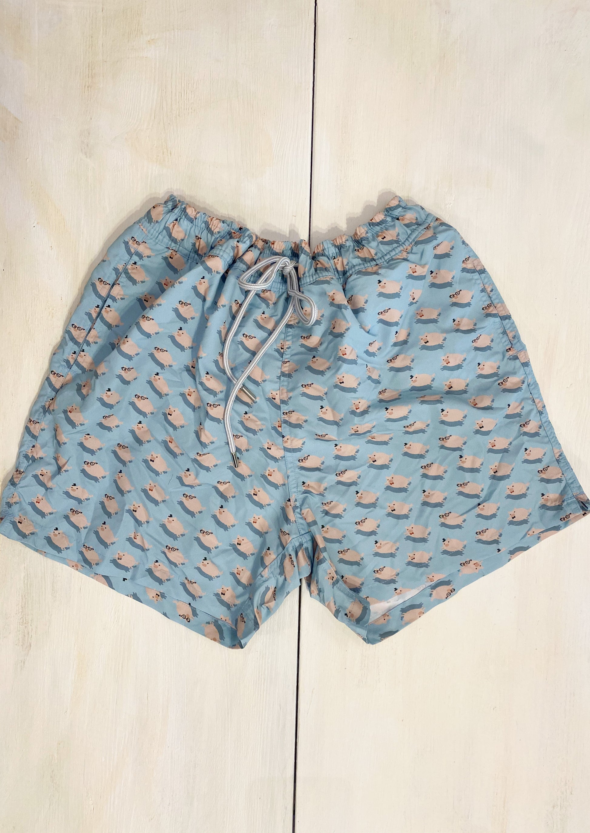Boxer uomo colore azzurro chiaro con piccoli maialini rosa. Elastico in vita e coulisse per regolare la larghezza. Tasca con bottone dietro .   